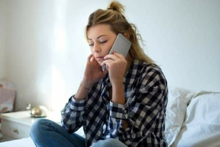 женщина разговаривает по телефону с испуганным лицом, рядом лежит телефон скорой помощи